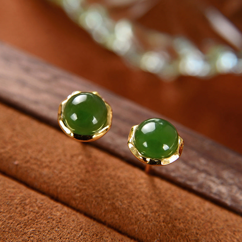Close up of small round green jade stud earrings with gold rim on wood background