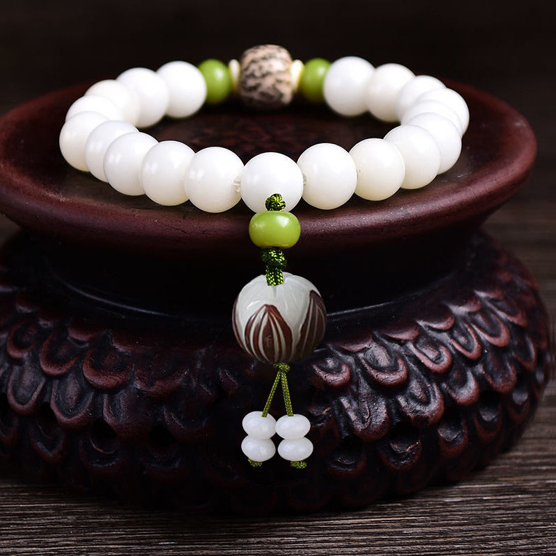 White bodhi seed bracelet with a carved lotus flower charm resting on a wooden stand