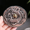 Close up of a round copper alloy incense burner with a raised dragon design holding a brass sphere.