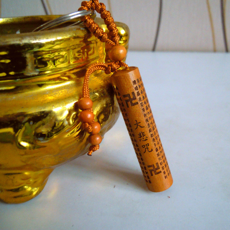 Close-up of a peach wood cylinder keychain with Chinese text engravings resting on a gold bowl.