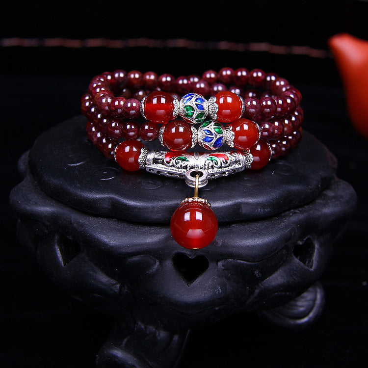 Deep red natural garnet wrap bracelet with red agate beads and a silver-tone pendant resting on a teapot