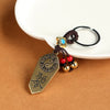 Close-up of a brass Bagua token keychain with red beads and a brown knotted cord.