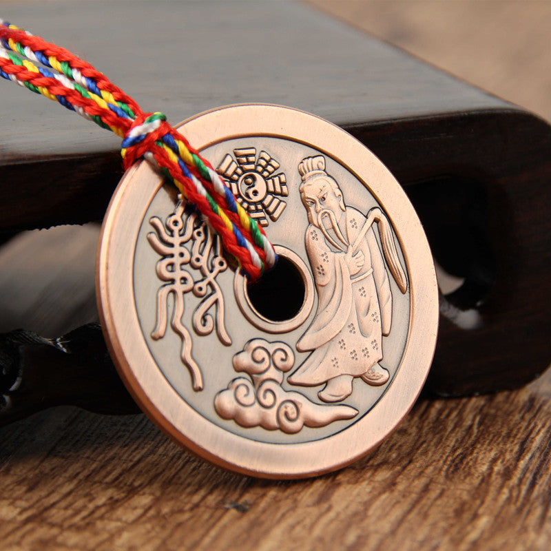 Close-up of a round copper pendant with an engraved figure and Chinese characters on a multi-colored rope