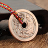 Close-up of a round copper pendant with an engraved figure and Chinese characters on a multi-colored rope