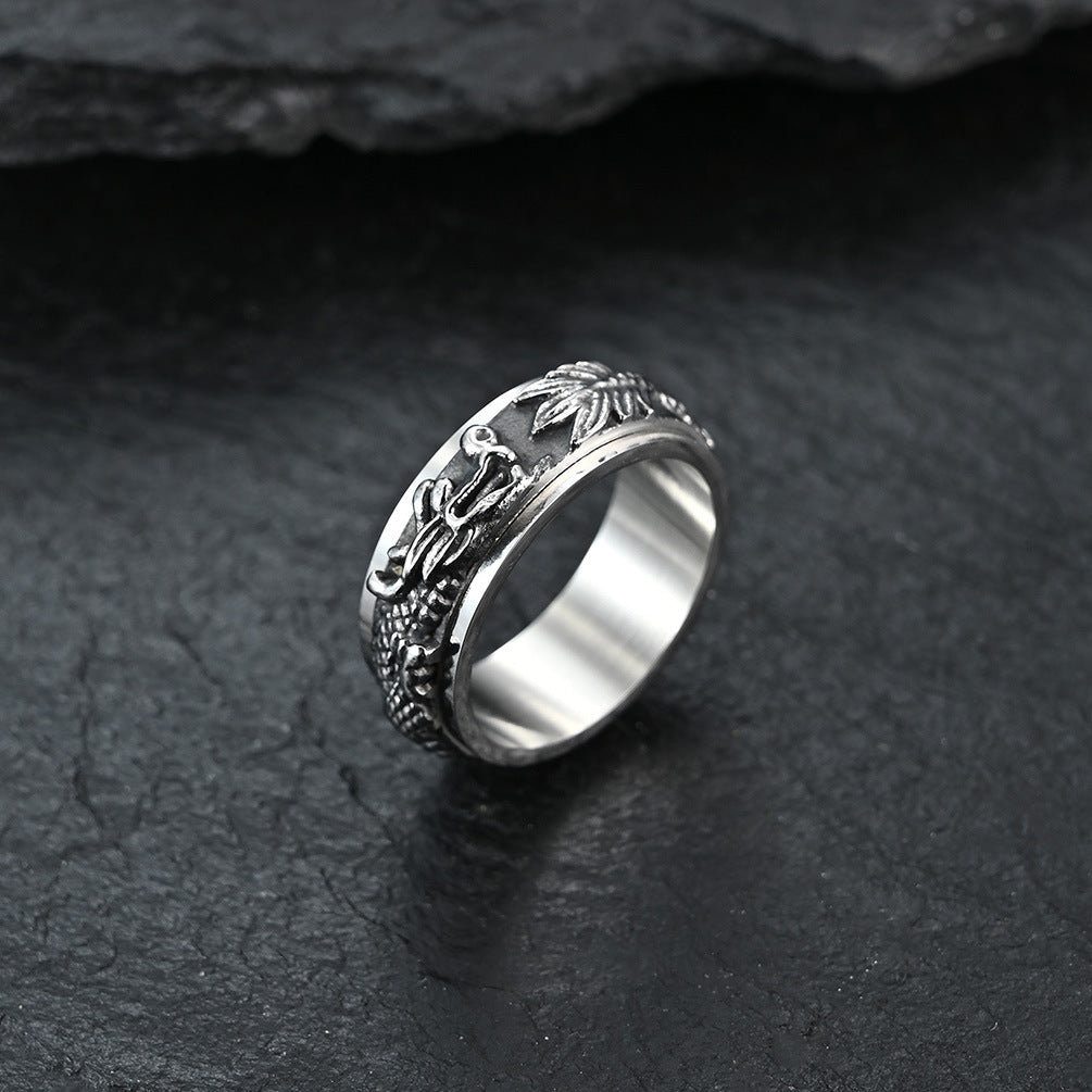 Close-up of a silver titanium steel ring with a raised dragon pattern on a dark stone surface
