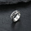 Close-up of a silver titanium steel ring with a raised dragon pattern on a dark stone surface