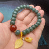 Hand wearing a green bodhi seed bracelet with white lotus charm and tassel