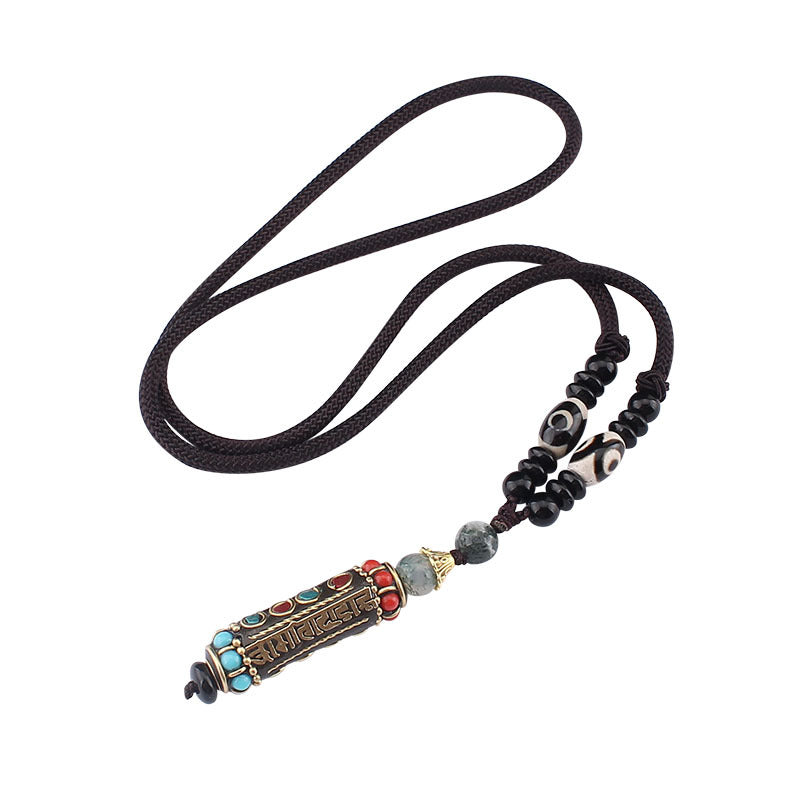 Close up of a cylindrical pendant with Tibetan script hanging on a dark brown cord