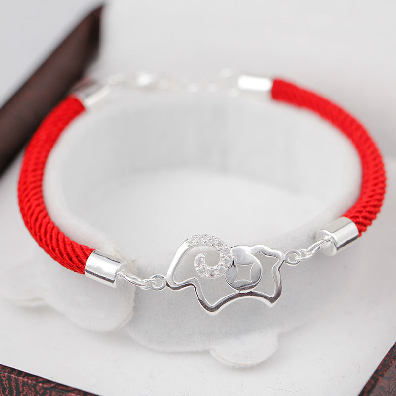 Close-up of a red braided bracelet with a silver goat charm on a white surface