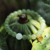 Close up of a green jade bracelet with a gold lotus pod charm resting on a seed pod