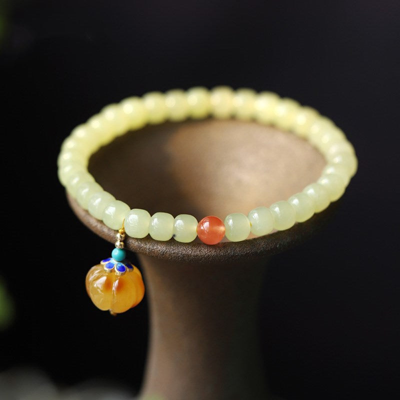 Pale green jade beaded bracelet with amber pumpkin charm on display stand