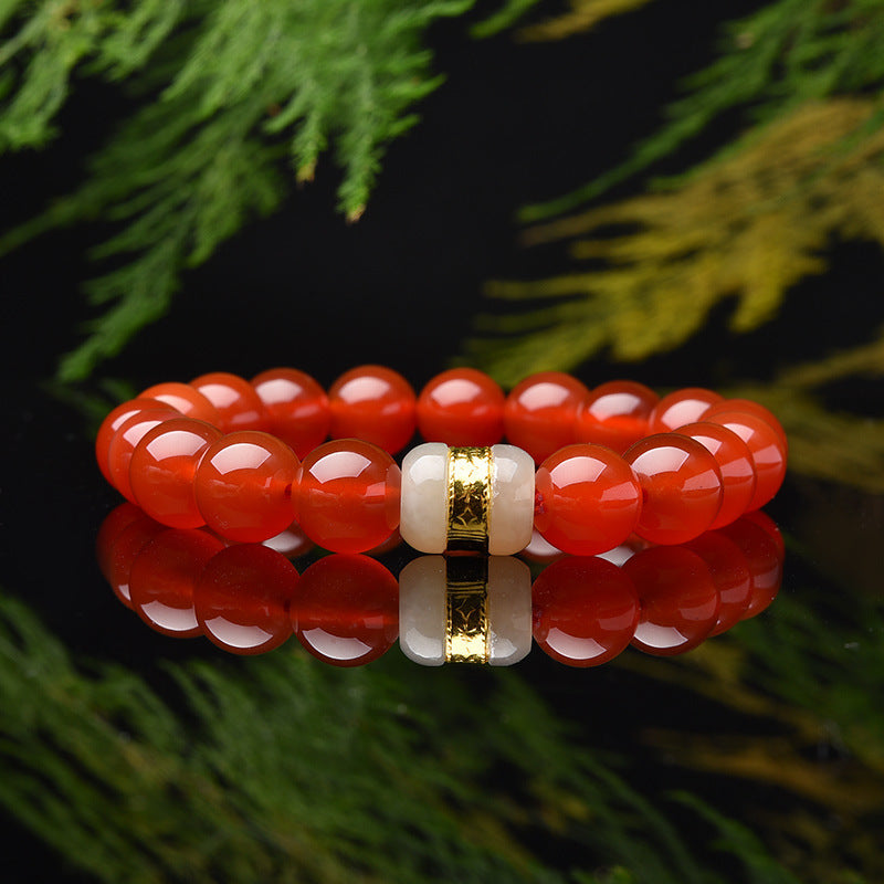 Red agate bead bracelet with white jade and gold-tone charm on a reflective surface