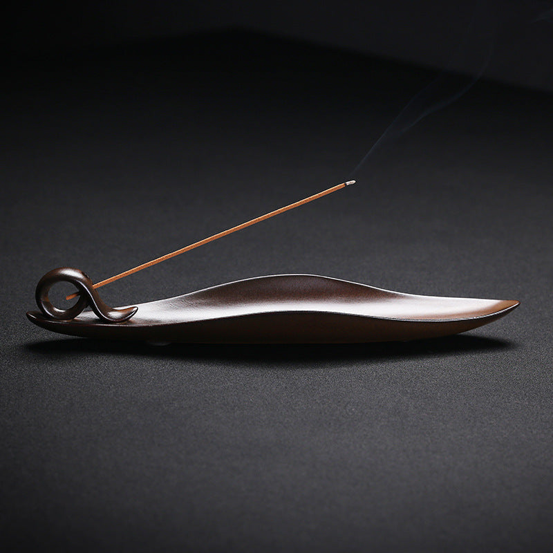 Brown ceramic leaf-shaped incense burner holding a stick of incense