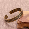 Antiqued copper open cuff bracelet with Tibetan script engraving resting on a wooden stand