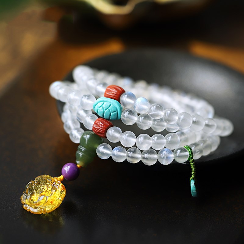 Coiled moonstone mala bracelet with carved amber lotus charm on dark surface