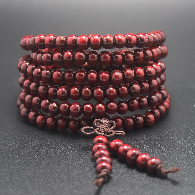 Red wooden mala bracelet with 108 beads wrapped around itself featuring a bow knot tassel
