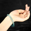 Light green natural jade bangle bracelet on a dark textured background