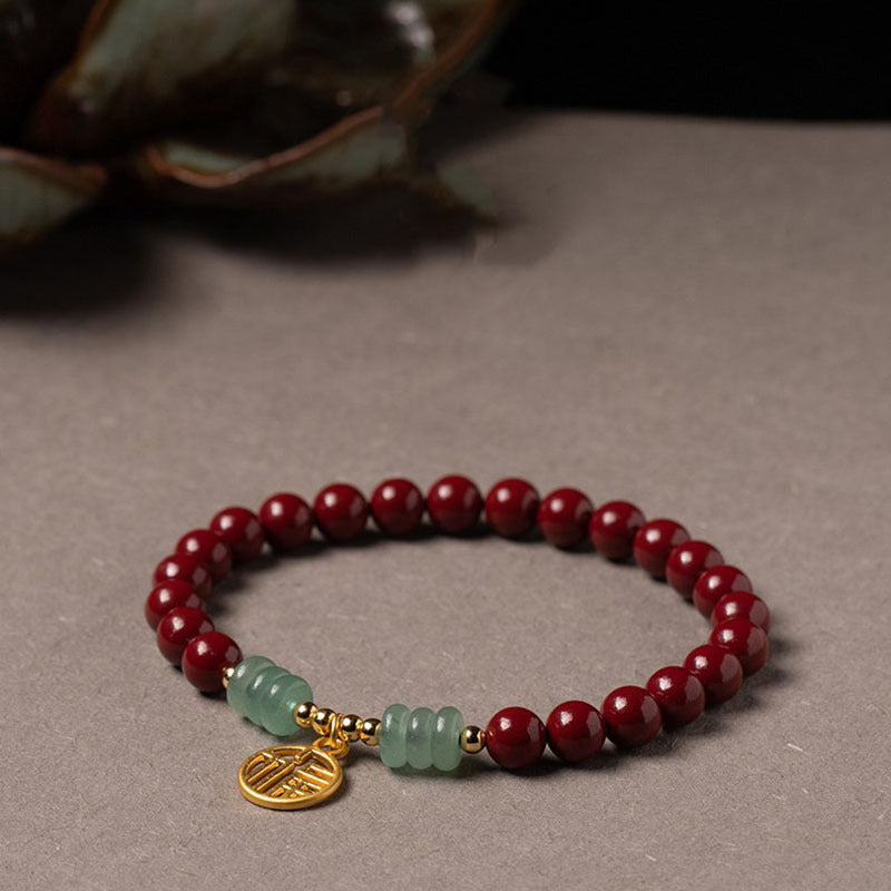 Red cinnabar beaded bracelet with a gold-tone Fu charm on a brown ceramic plate