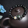 Close up of an obsidian beaded bracelet with a fox charm resting on a teapot