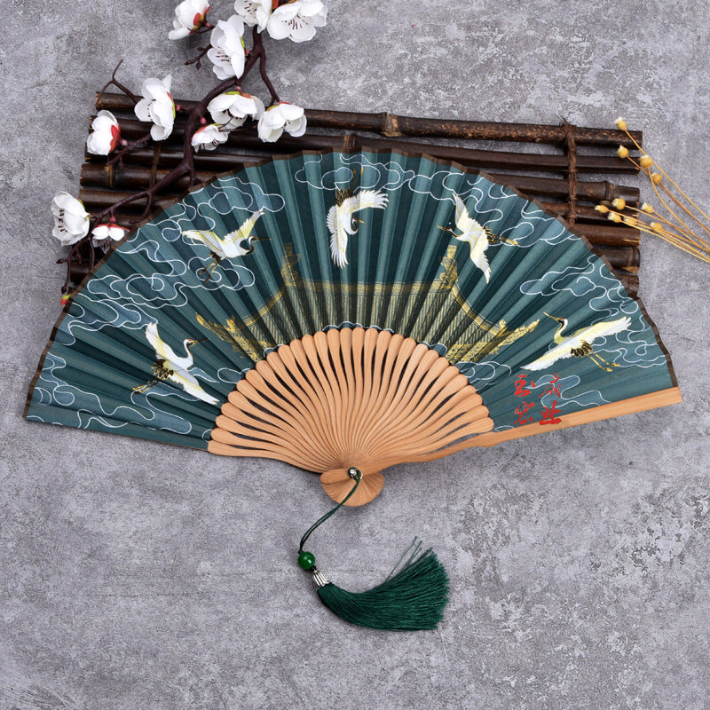 Open handheld folding fan with green silk cloth featuring white cranes and clouds on a bamboo frame