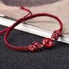 Close-up of a red woven bracelet with a central Cinnabar coin charm and two Pixiu figures