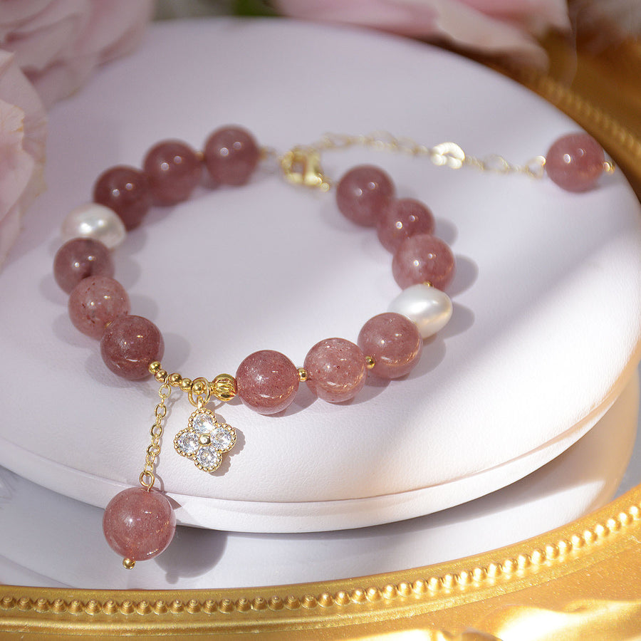 Pink strawberry quartz bracelet with white pearls and a clover charm on a white dish