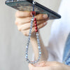 Close up of a phone strap with grey moonstone and red cinnabar beads hanging from a smartphone.