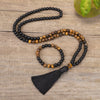 A handmade mala necklace and bracelet set made of tiger eye and black stone beads on a wooden surface