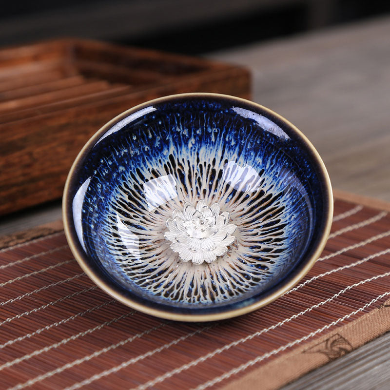Close up of a blue glazed ceramic tea cup with a silver lotus flower design inside