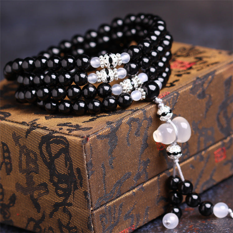 Close up of a black agate 108 bead bracelet wrapped around a box with a white gourd charm