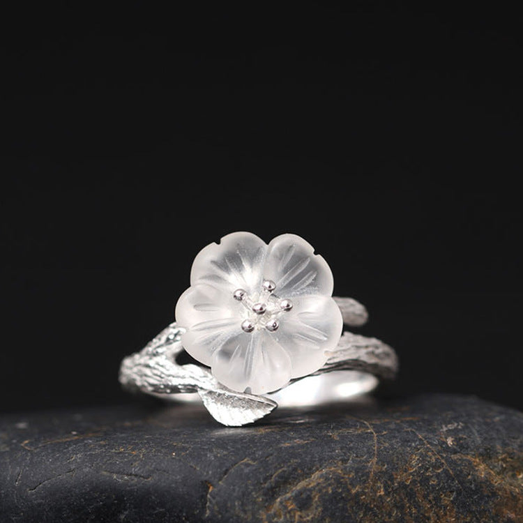 Close-up of a sterling silver ring with a white crystal plum blossom flower on a dark background