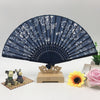 Blue handheld folding fan with white floral print displayed on a wooden stand