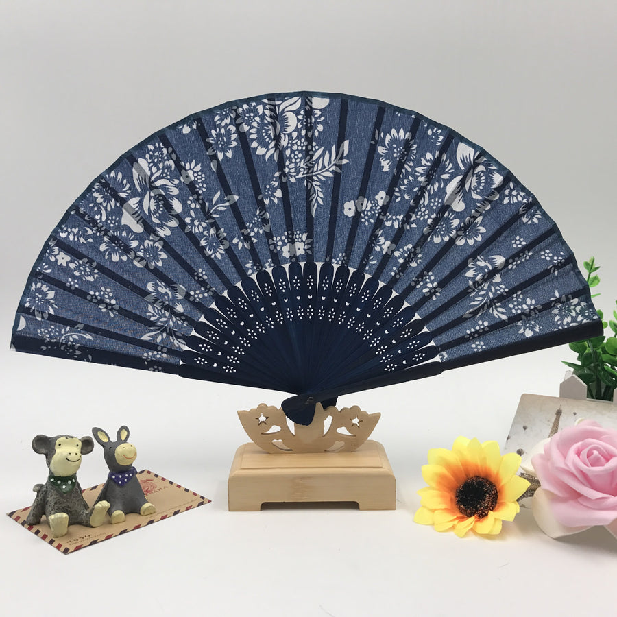 Blue handheld folding fan with white floral print displayed on a wooden stand