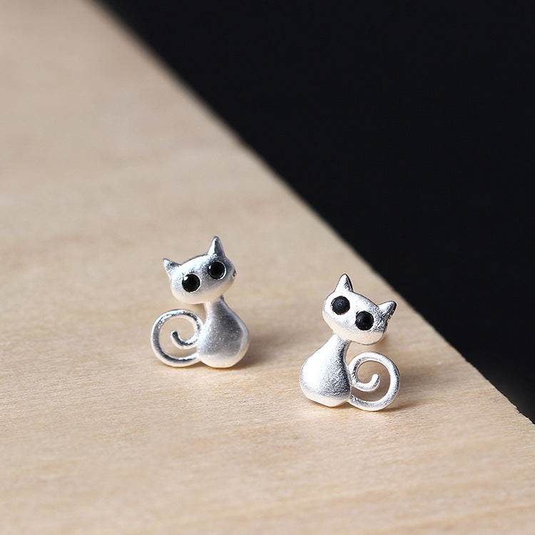 Pair of small silver cat stud earrings on a wooden surface