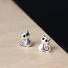 Pair of small silver cat stud earrings on a wooden surface