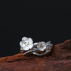 Close up of a silver ring with two white flowers and gold centers on a wood surface