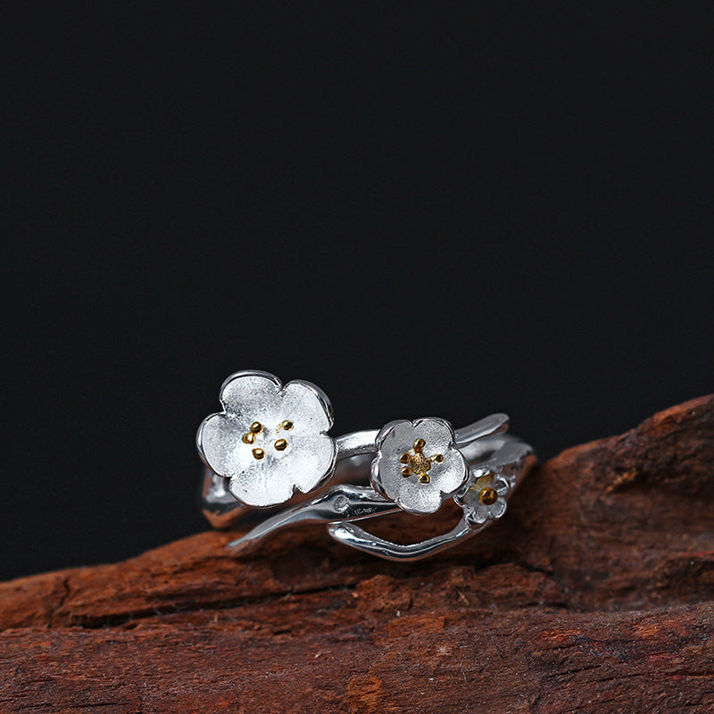 Close up of a silver ring with two white flowers and gold centers on a wood surface