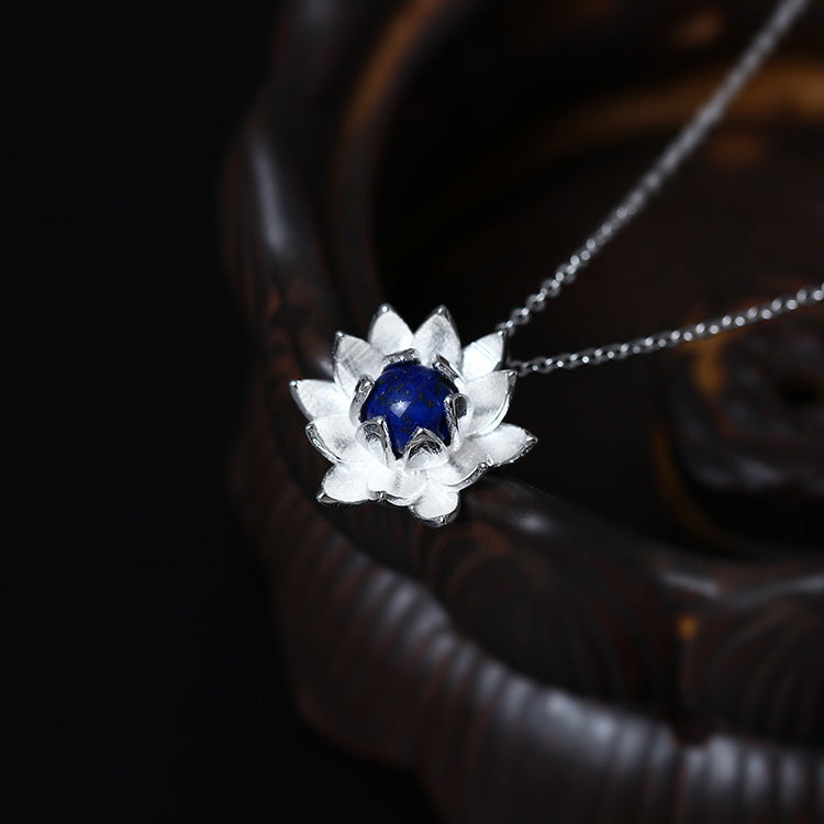 Close up of a silver lotus flower pendant with a blue lapis lazuli stone on a silver chain.