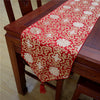 Red Chinese silk table runner with gold floral pattern and tassel on a wooden table