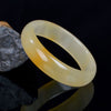 Polished natural golden silk jade bangle with yellow and white coloring on a dark background
