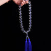 Hand holding a loop of clear white crystal beads with blue tassels against a black background