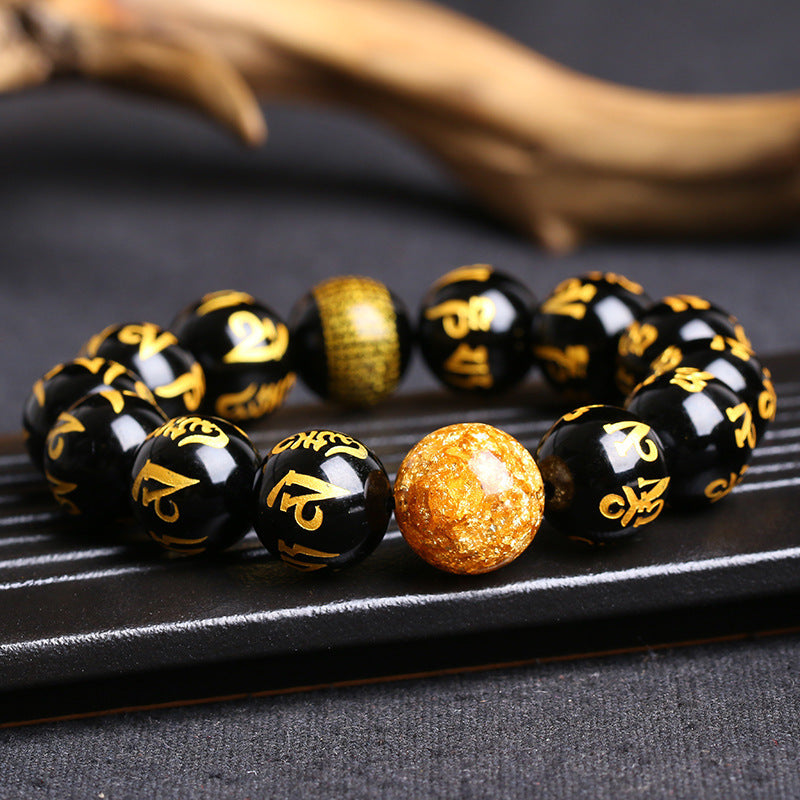 Close up of black bracelet with gold mantra script and a textured gold foil bead