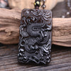 Rectangular black obsidian pendant with a carved dragon design resting on wood