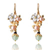 Pair of gold-tone floral drop earrings with pearl and stone accents hanging against a dark background.