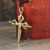 Close up of a handmade copper vajra pendant hanging from a black cord against a red wooden background.