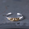 Close up view of a silver ring with a gold lotus flower design on a grey stone surface