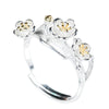 Close up of a silver ring shaped like a branch with three white flowers and gold centers