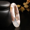 Close up of a translucent white and pink sakura agate bangle leaning against a dark stone object