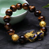 Close up of a brown Tiger Eye bead bracelet with a gold Pixiu charm resting on a dark stone surface