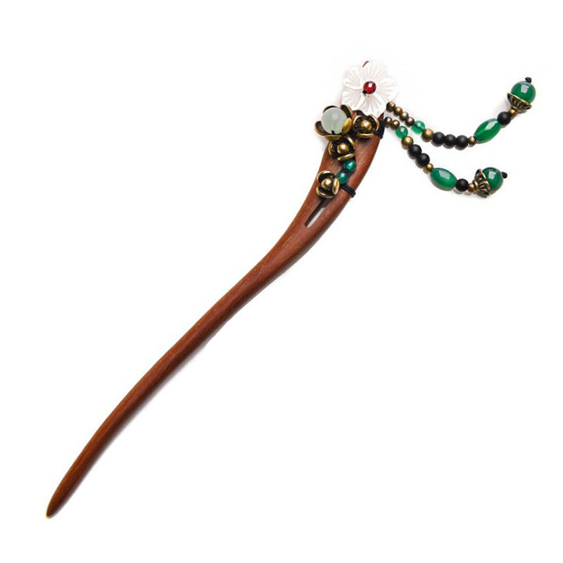 Close up view of a handmade wooden hairpin with a white flower and green beads on dark hair